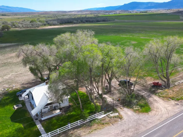 Aerial property view featuring a white-sided residence with a metal roof, surrounded by mature trees