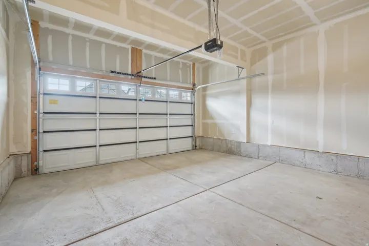 Concrete flooring, white paneled garage door with upper window inserts, automatic garage door opener, and unfinished drywall walls