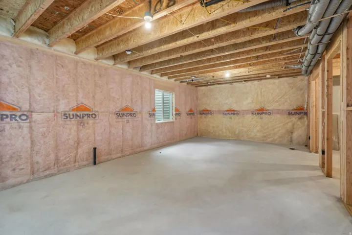 Unfinished basement with exposed ceiling joists, concrete flooring, and insulated walls