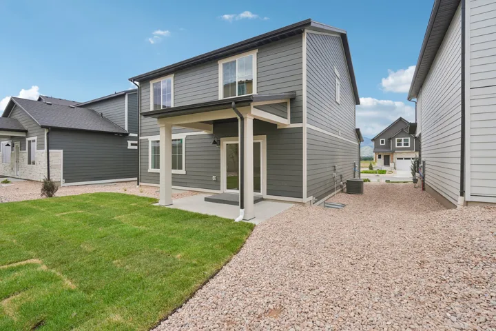 Two-story residence with gray siding, a covered patio, and a grassed yard area