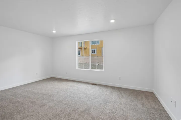 Recessed ceiling lighting, neutral carpeting, white interior walls, and a large window