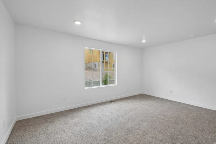 Recessed ceiling lighting, white painted walls, gray carpet flooring, and a white-framed window
