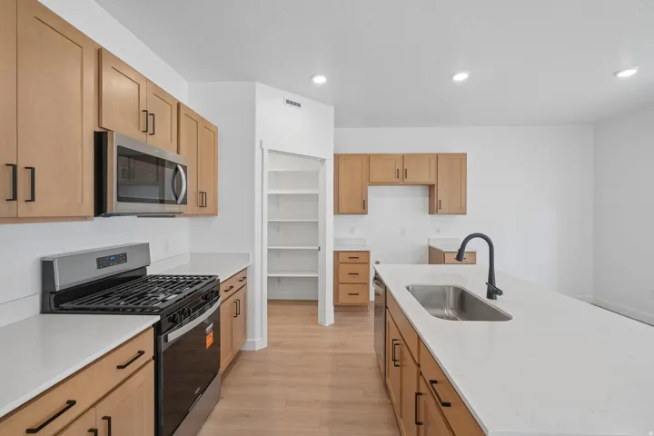 Kitchen featuring light wood-finish cabinetry, stainless steel appliances, a center island with an undermount sink, and recessed lighting