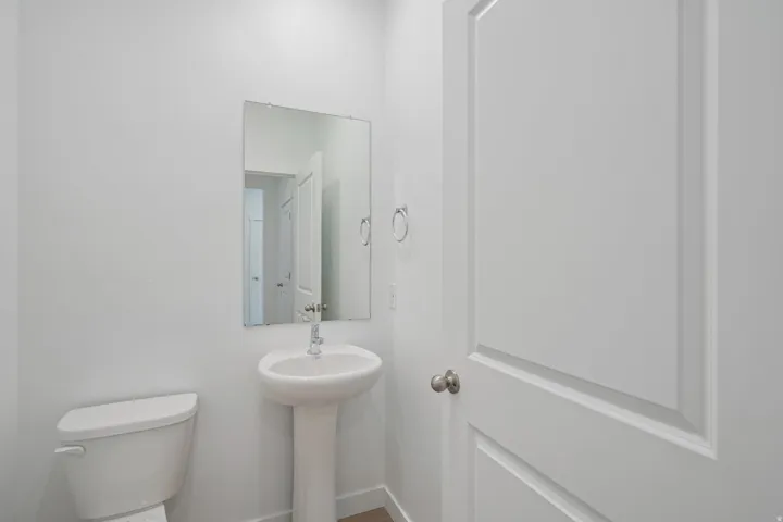 Pedestal sink with chrome faucet, wall-mounted rectangular mirror, and white paneled door with brushed nickel hardware