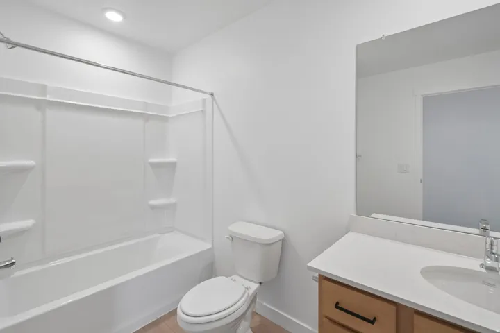 Bathroom featuring a built-in tub with shower, single vanity with a white countertop, and wood-finish flooring
