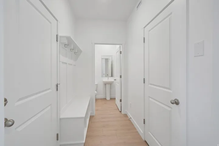 Hallway featuring built-in white storage bench with coat hooks, light wood-finish flooring, and white interior doors