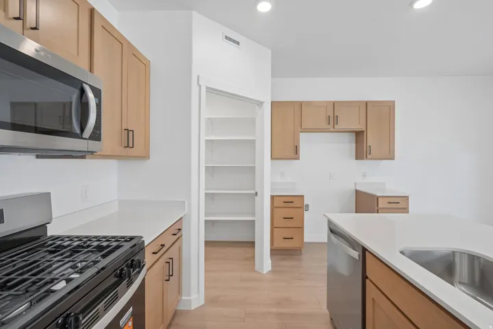 Kitchen featuring light wood-finish cabinetry, white countertops, a stainless steel microwave, and a gas range