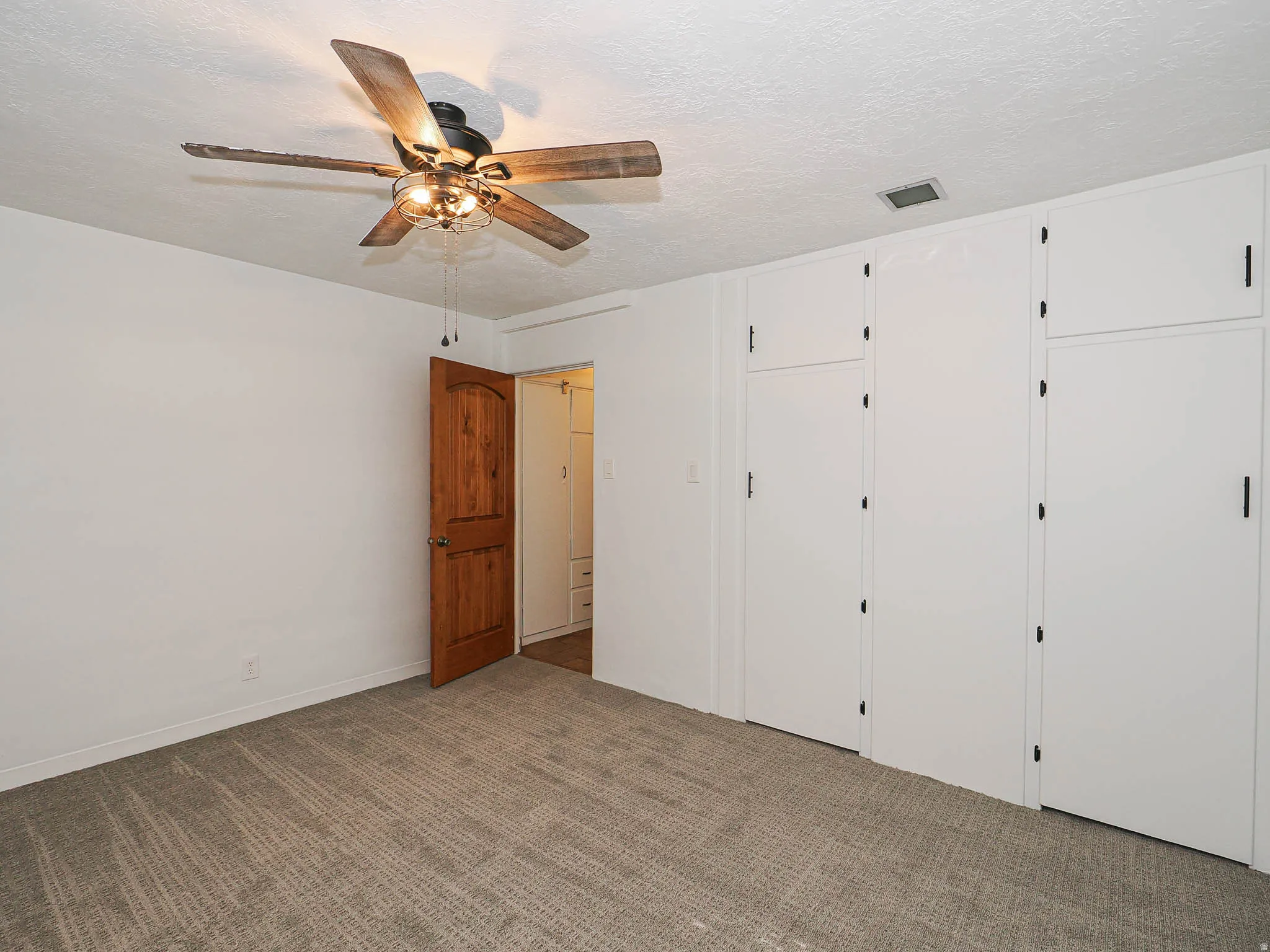 Spacious room featuring new carpeting, a rich wood-paneled door, and a full wall of built-in cabinetry with black hardware