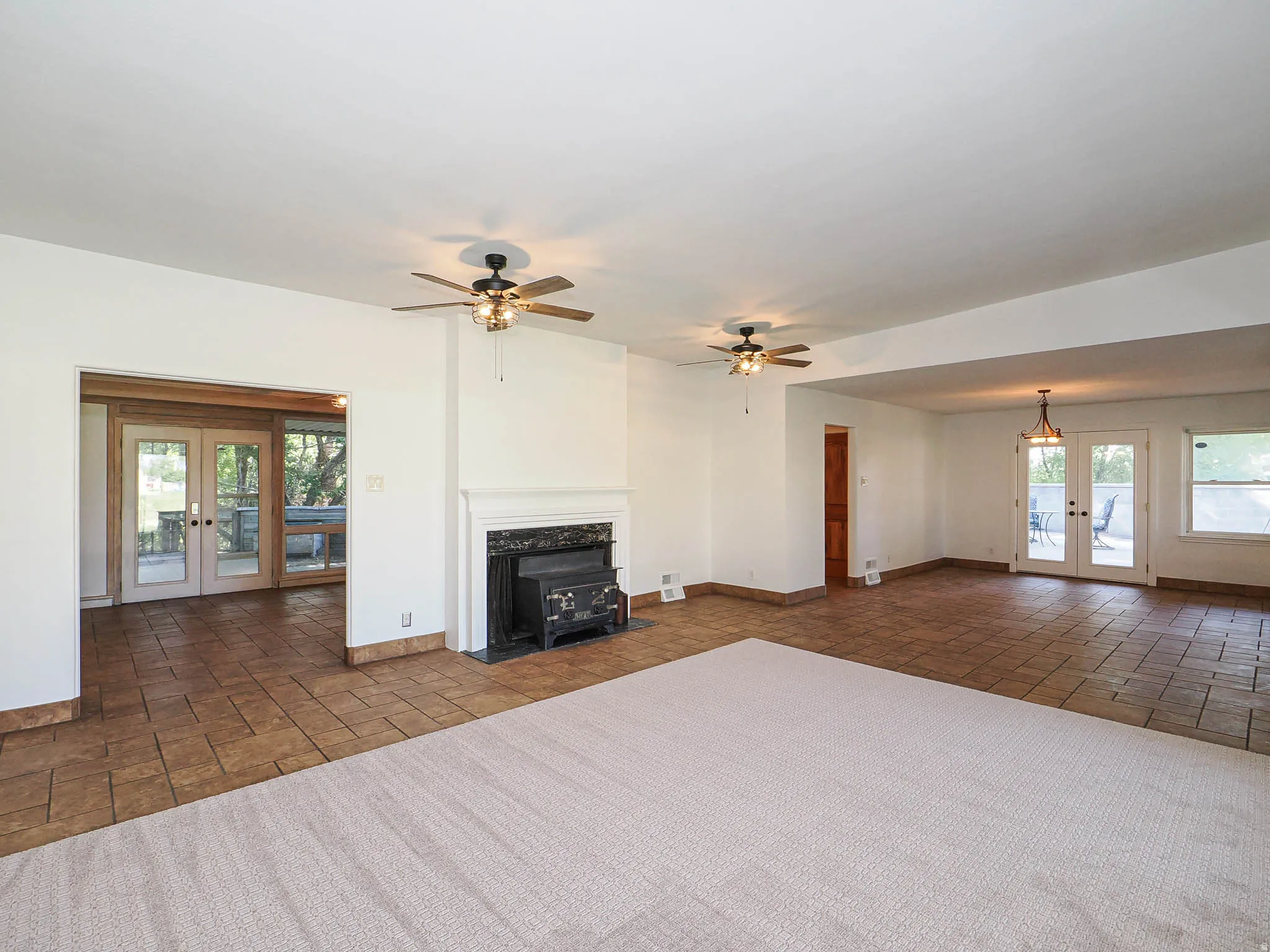 Expansive interior space featuring a central fireplace with an ornate mantelpiece, two ceiling fans with integrated lighting, and a combination of wall-to-wall carpeting and tiled flooring