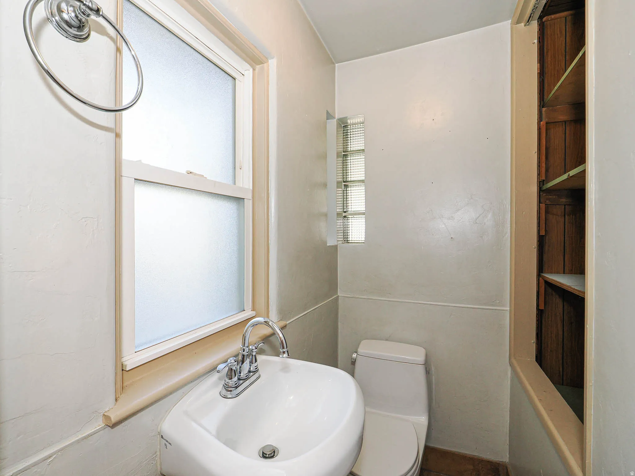White pedestal sink with chrome faucet, complemented by a frosted window and glass block accent