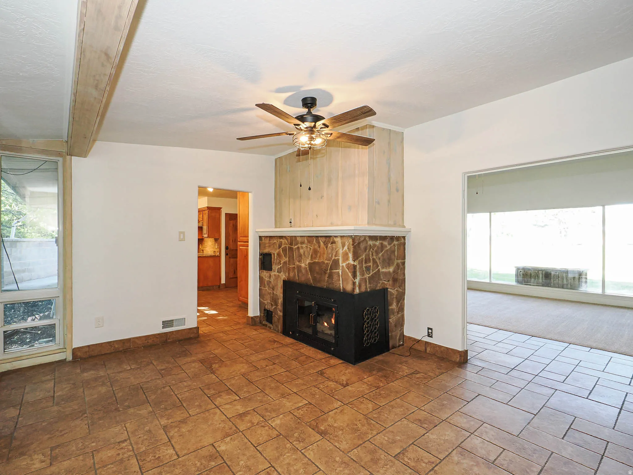 Living space featuring stone-clad fireplace with wood-paneled facade, tile flooring, and a ceiling fan