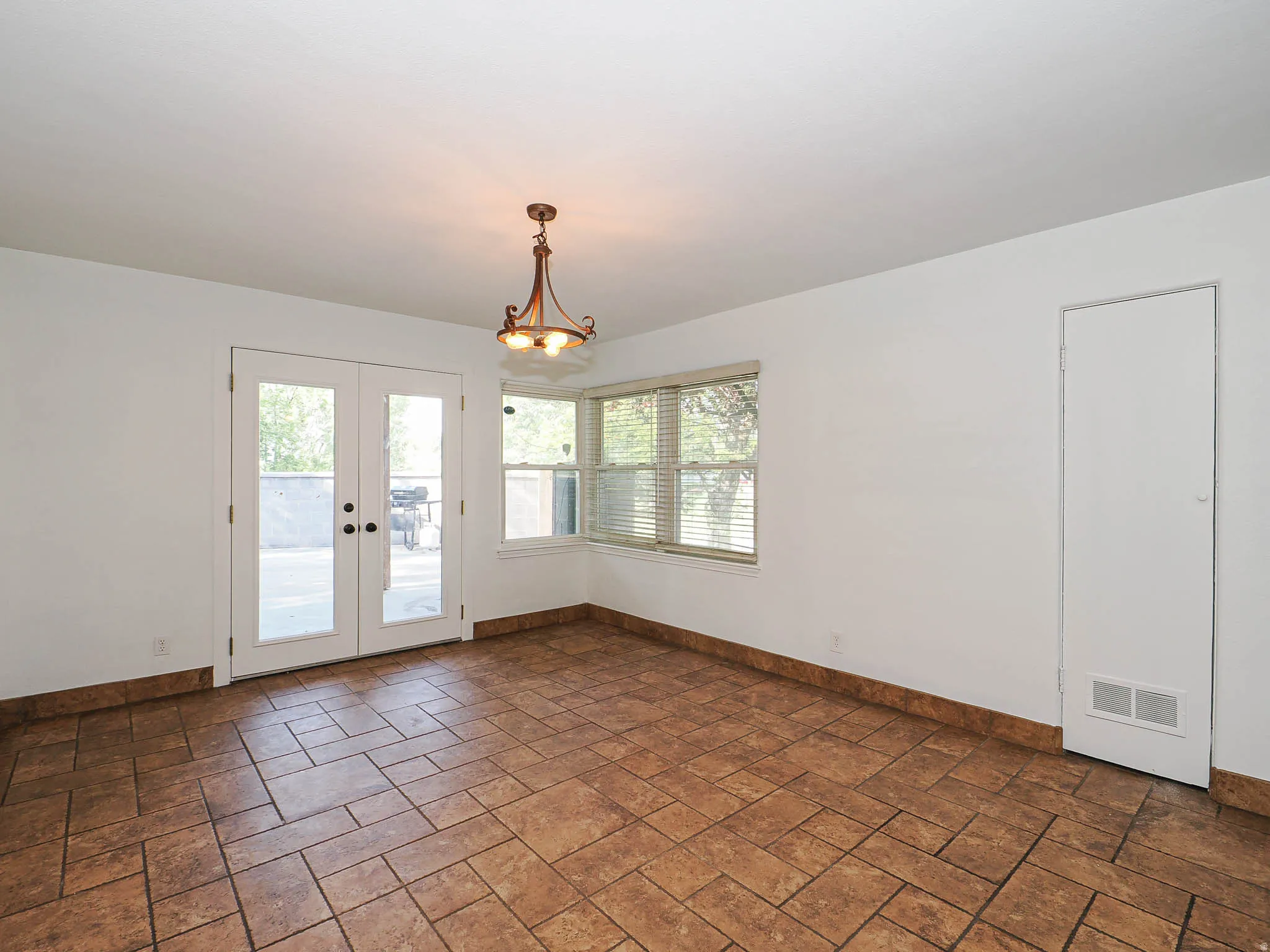 Spacious room featuring tile flooring, white walls, and a multi-bulb chandelier
