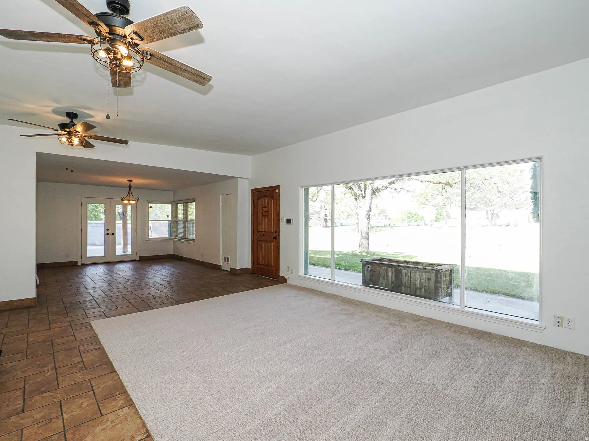 Spacious interior featuring a large picture window, light-toned carpeting, and two ceiling fans with integrated lighting