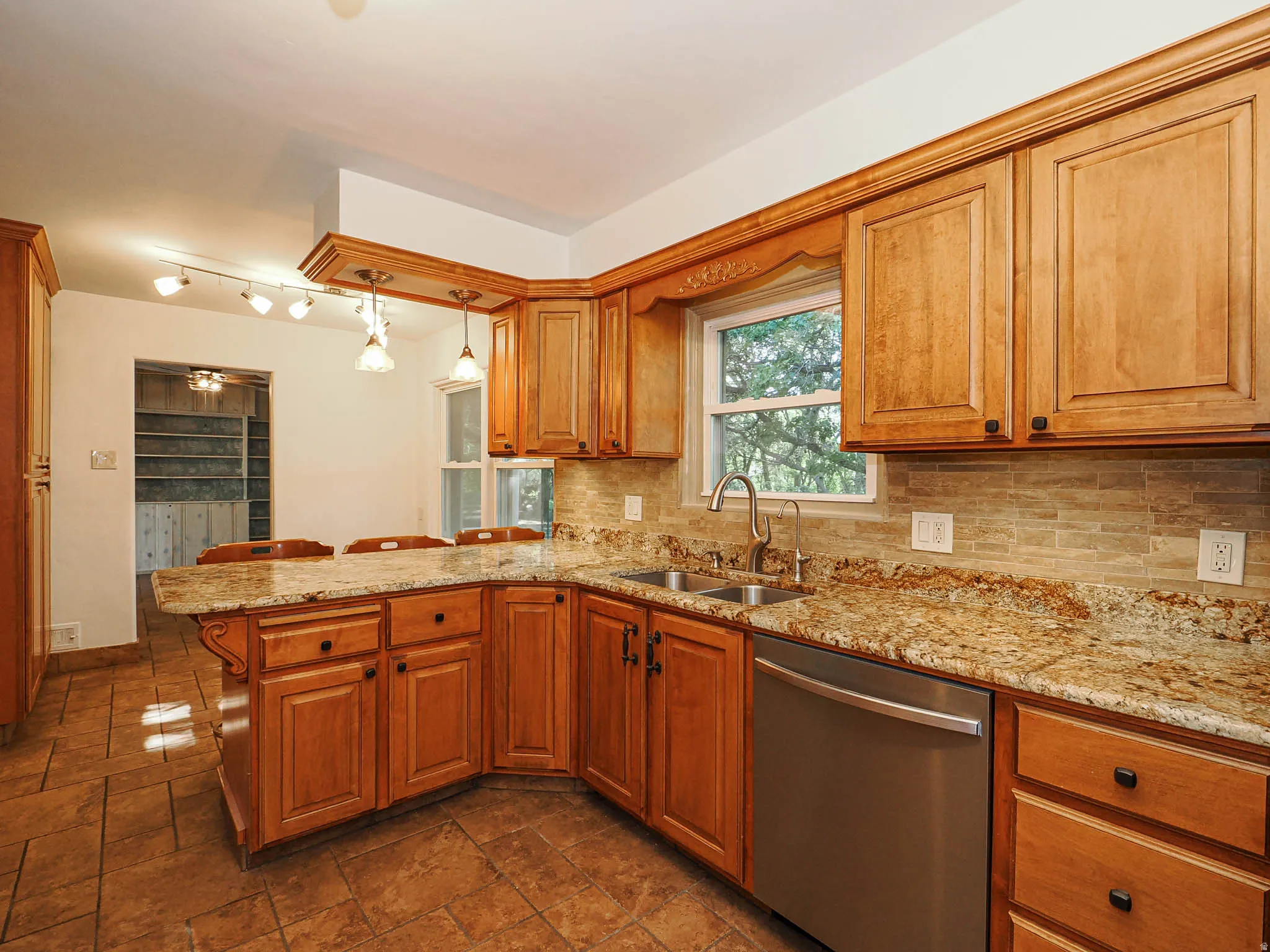 Kitchen featuring wood cabinetry, granite countertops, tile flooring, a stainless steel dishwasher, and a stone-finish backsplash