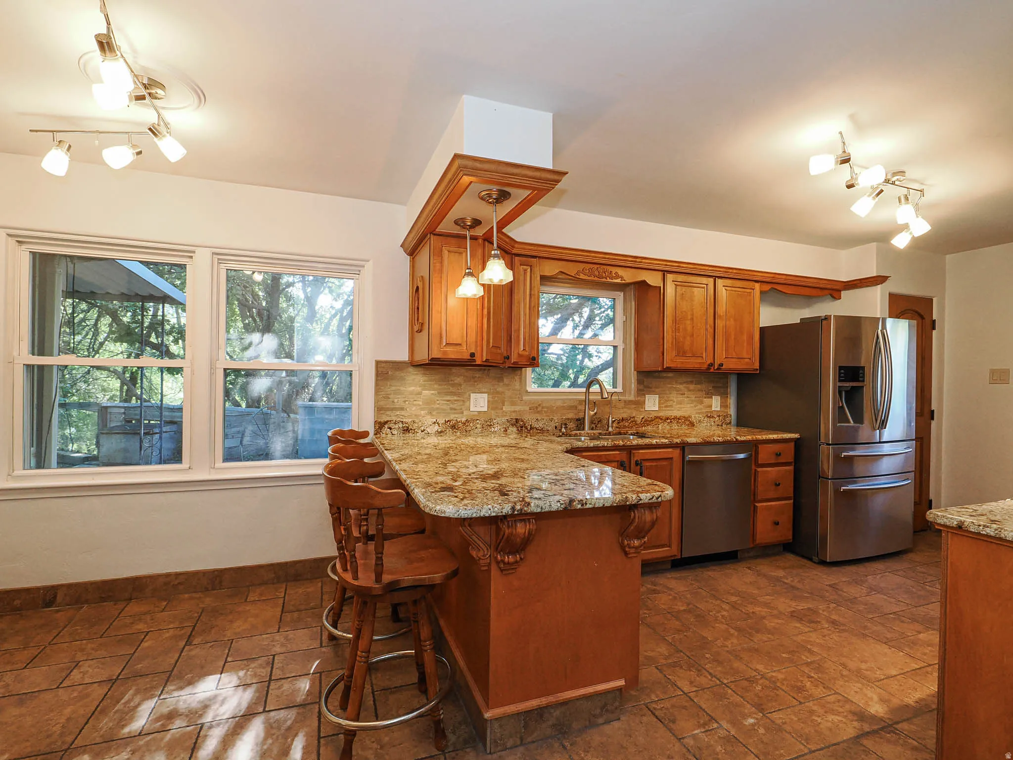 Kitchen featuring a granite-topped island with seating, natural wood cabinetry, stainless steel appliances, and a tile backsplash