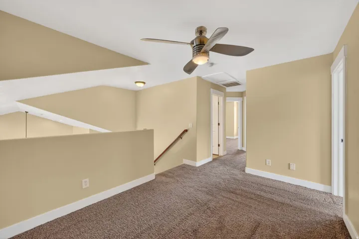 Upper landing featuring a ceiling fan, plush carpet, white trim, and a staircase with a wood handrail