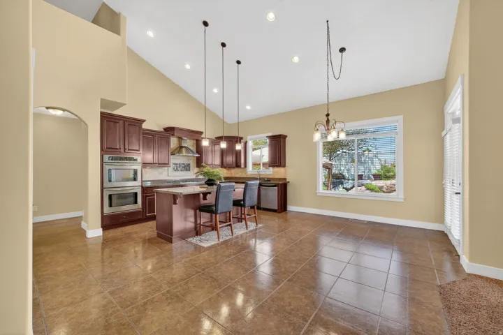 Kitchen and dining area featuring vaulted ceilings with recessed lighting, brown tile flooring, dark wood cabinetry, a central island with bar seating, and stainless steel appliances