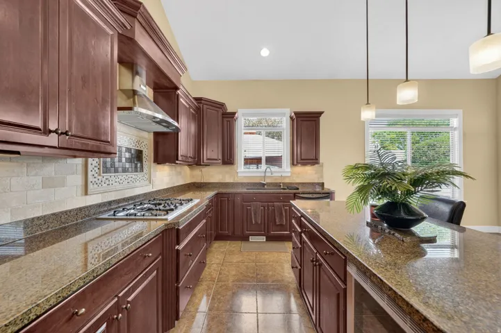Kitchen featuring wood cabinetry, granite countertops, an undermount sink, a built-in gas range with a stainless steel range hood, and tile flooring