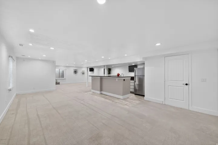 Spacious finished lower level featuring recessed lighting, light-toned carpet, a built-in wet bar with a dark countertop, stainless steel refrigerator, and paneled interior doors