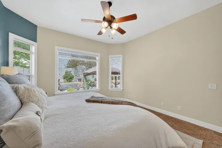 Bedroom featuring a ceiling fan with integrated lighting, multiple windows with blinds, a contrasting accent wall, and neutral-toned wall paint