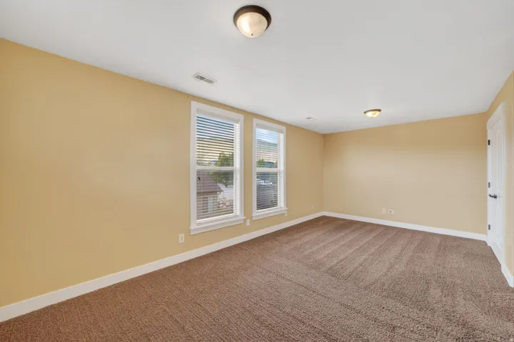Spacious room featuring neutral tone walls, two prominent windows with blinds, and recessed lighting fixtures