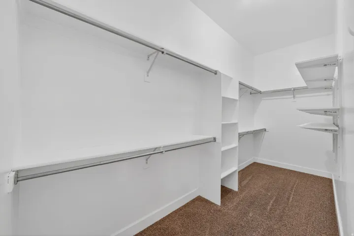Master Bedroom walk-in closet featuring built-in shelving, multiple hanging rods, and brown carpet flooring