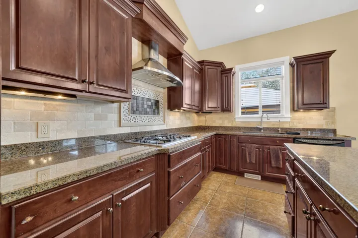 Kitchen featuring rich wood cabinetry, granite countertops, and a tiled backsplash