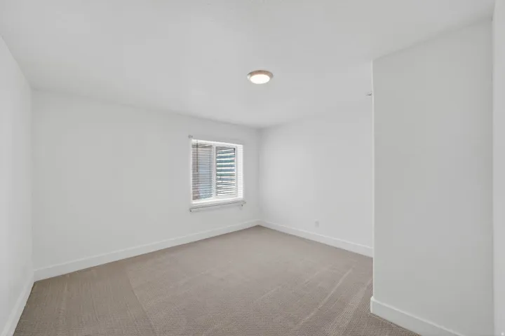Bright interior space featuring a window with horizontal blinds, neutral carpeting, white walls, and a ceiling-mounted light fixture