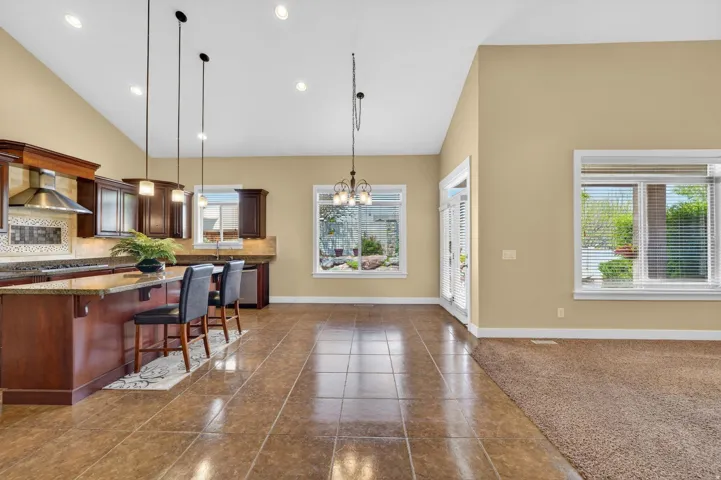Spacious kitchen and living area featuring a vaulted ceiling, recessed lighting, and a blend of tile flooring and carpet