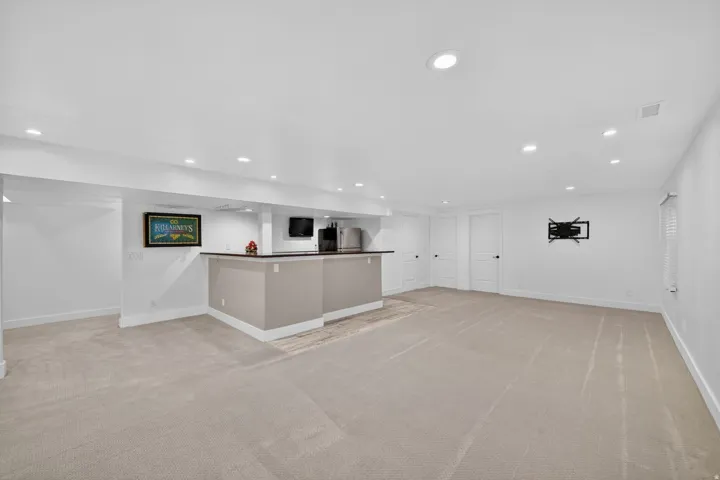 Expansive carpeted room featuring a built-in bar with a dark countertop, recessed lighting, and multiple white panel doors