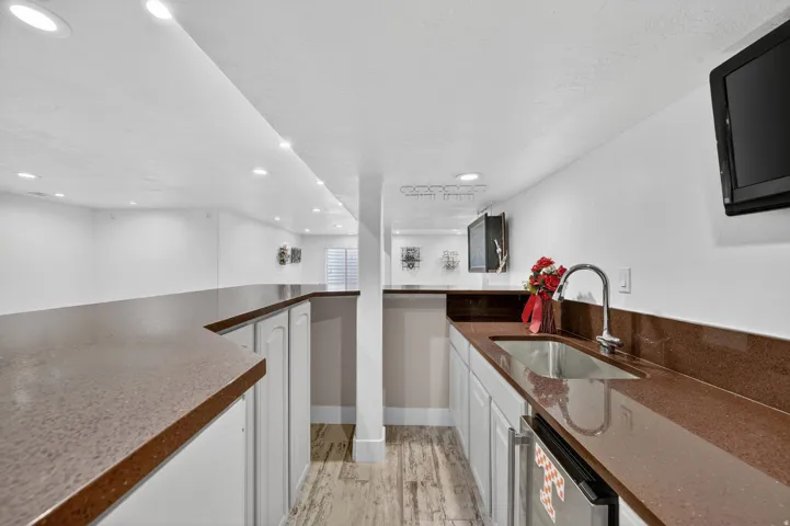 Full wet bar featuring a stainless steel sink, gooseneck faucet, light cabinetry, and rich countertop