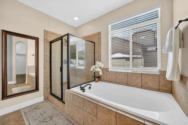 Master Bathroom featuring a tiled soaking tub with deck-mounted fixtures, a glass-enclosed shower with a black frame, and neutral wall tile