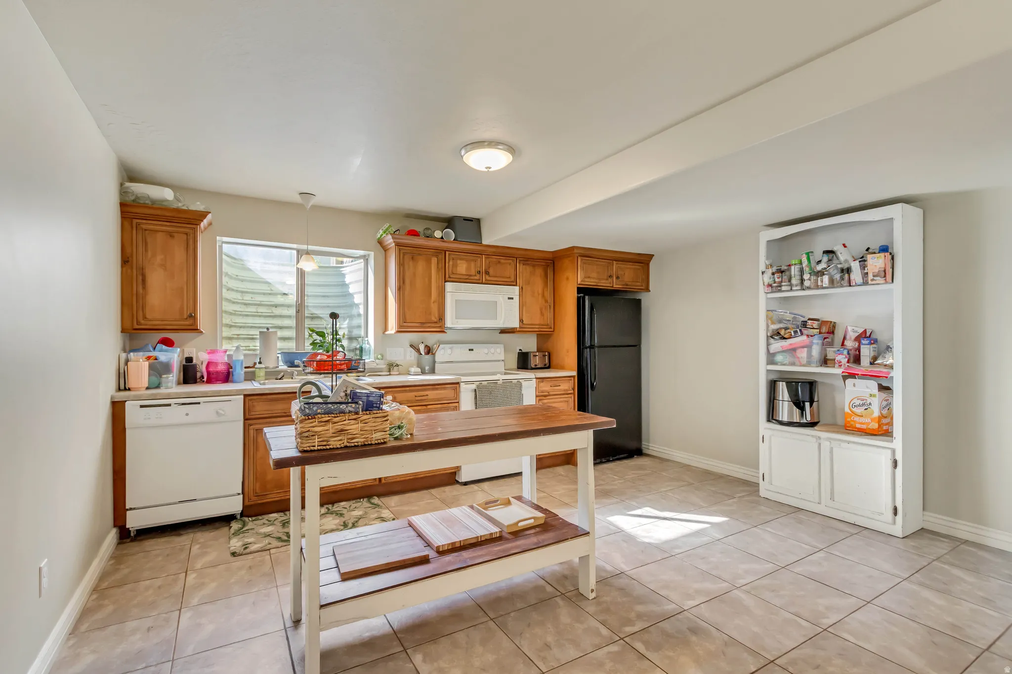 Kitchen featuring wood cabinetry, white appliances, and light-toned tile flooring