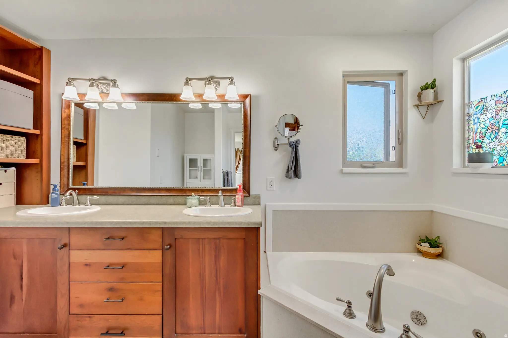 Dual vanity with wood cabinetry and countertop, framed mirror, and integrated soaking tub
