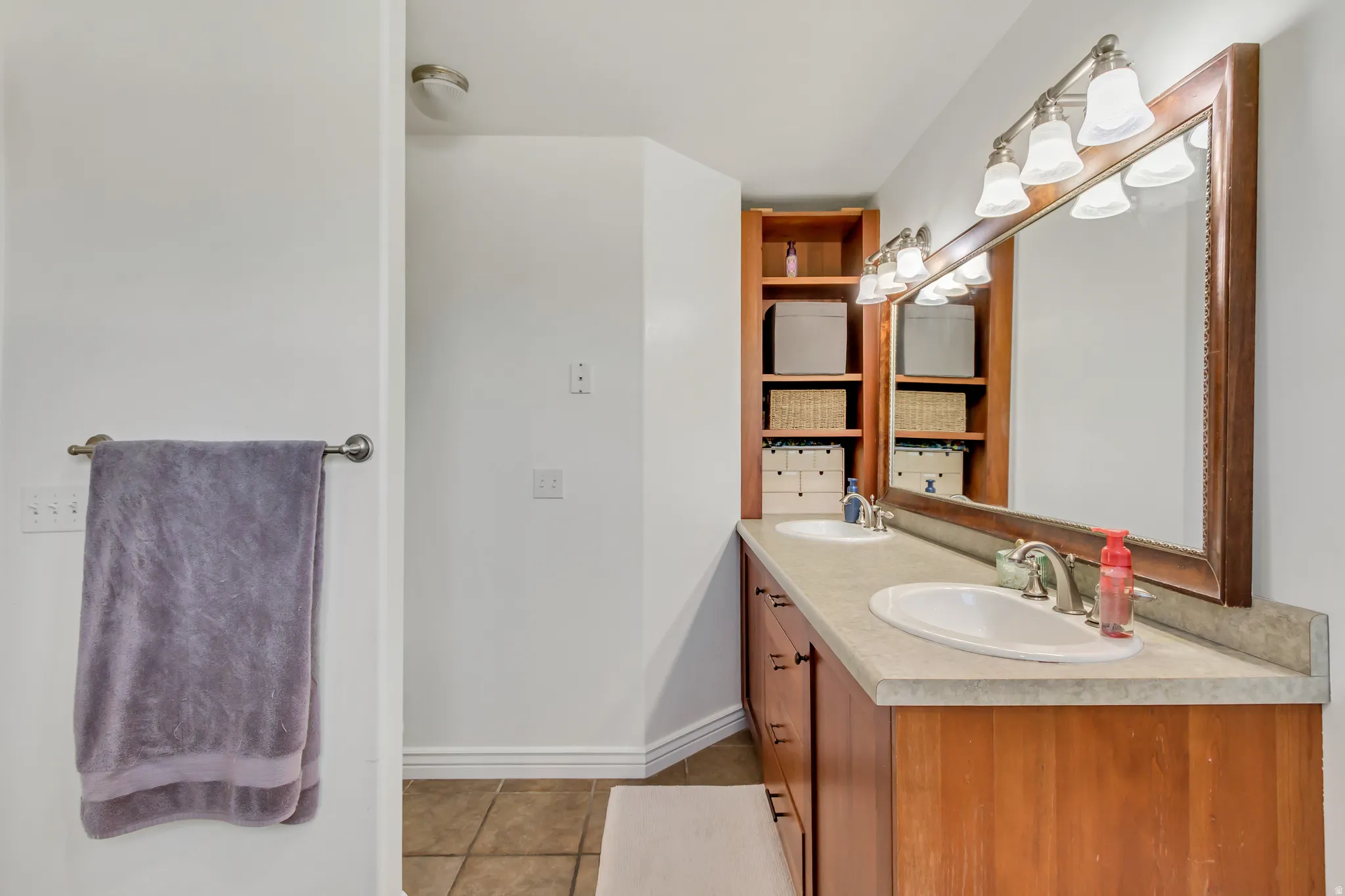 Double vanity with integrated sinks, a wide framed mirror, and warm wood-finish cabinetry