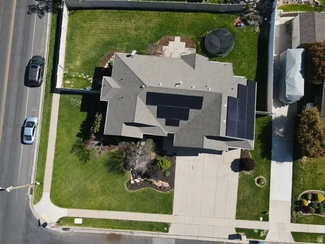 Aerial view showcasing the property with a gray shingle roof, solar panel installation, a concrete driveway, and a fenced backyard