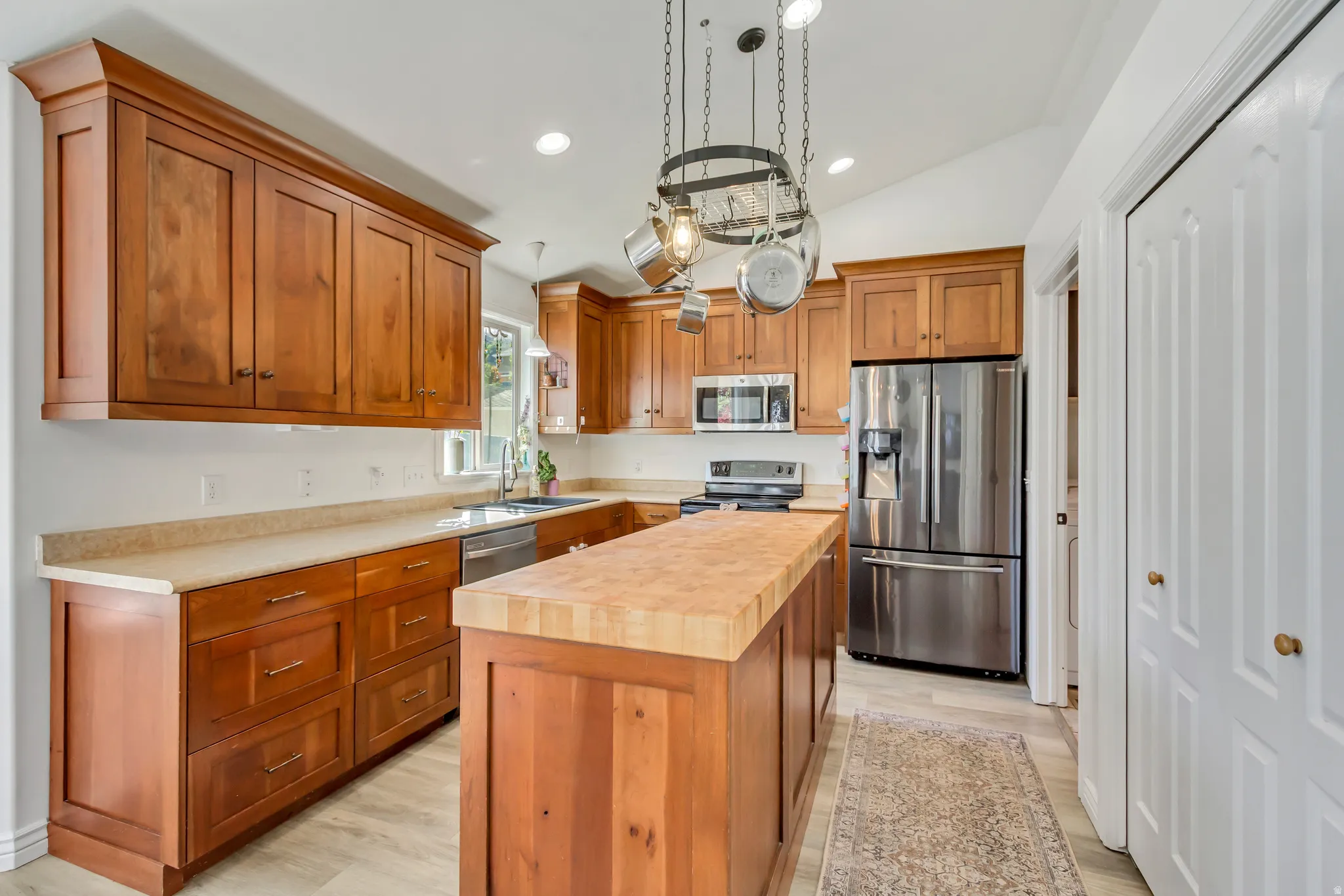 Kitchen featuring wood cabinetry, light-toned countertops, stainless steel appliances, a center island with a wood-finish top, and vaulted ceilings