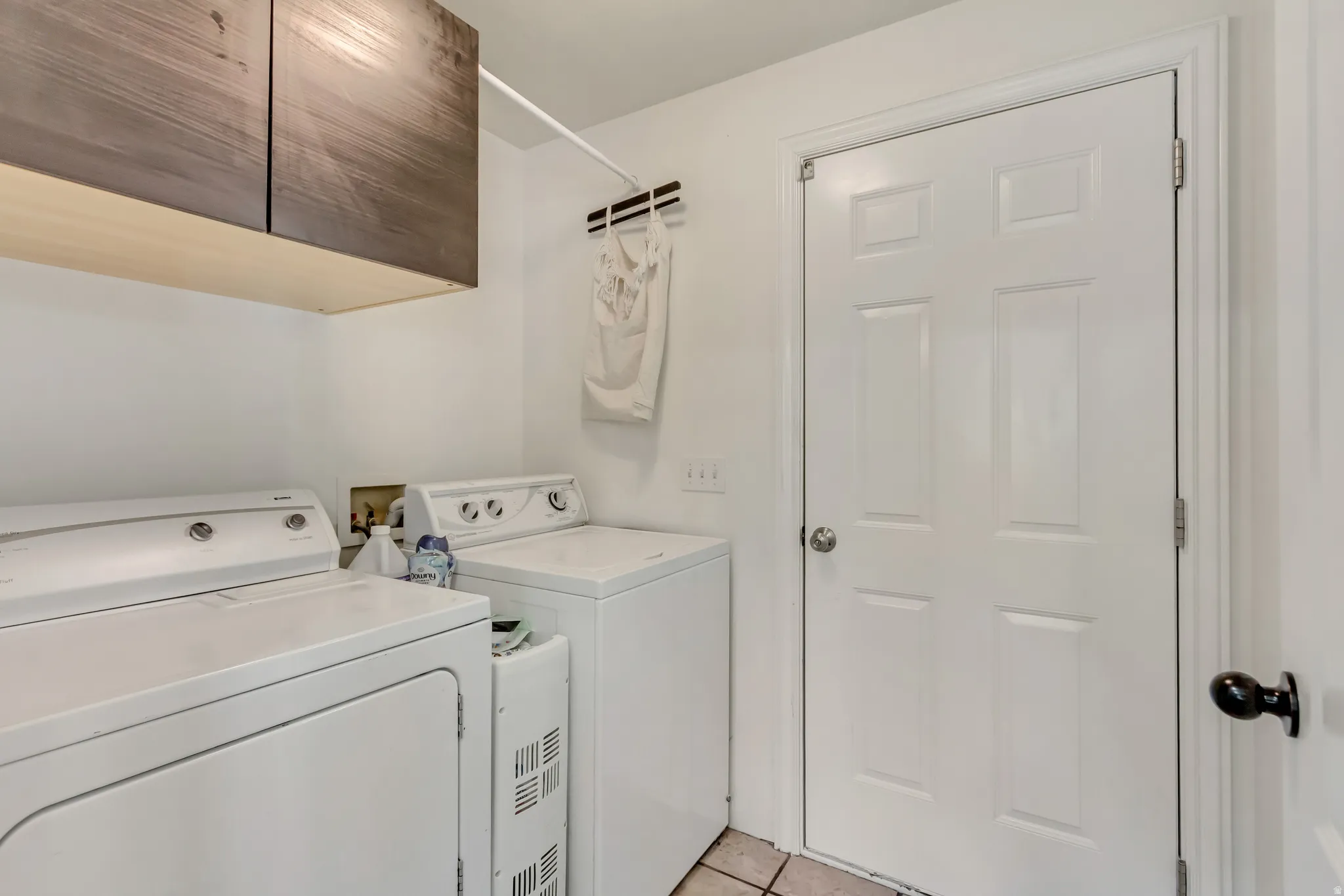 Laundry area featuring wood-finish upper cabinetry, a white panel door, and tile flooring