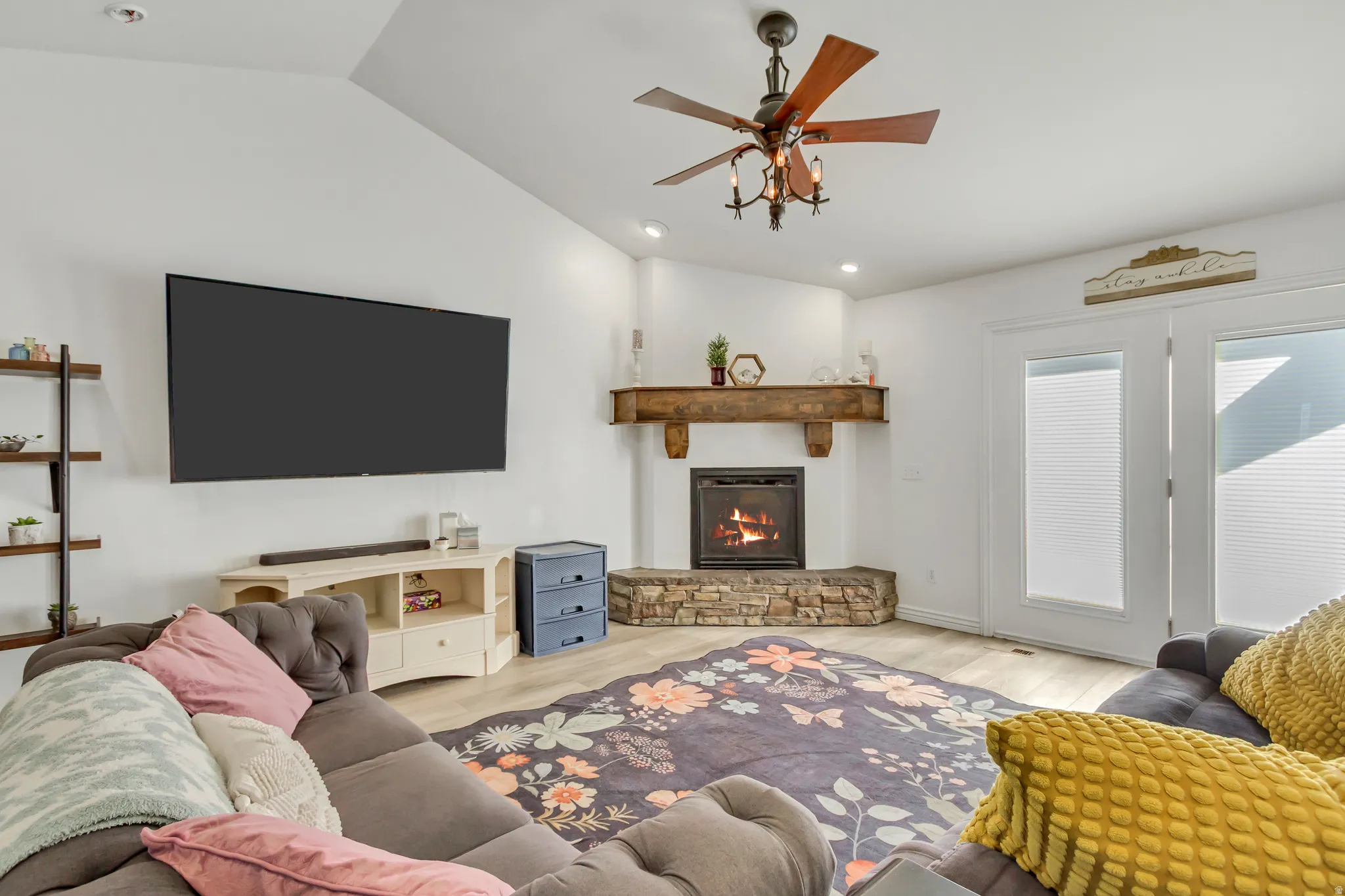 Living area featuring a stone surround fireplace with a wood mantle, vaulted ceilings, and wood-finish flooring