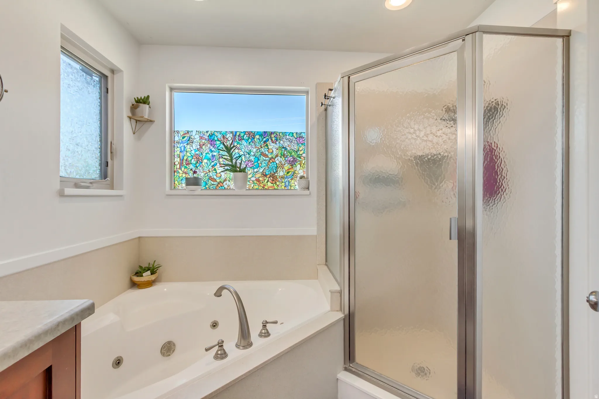 Bathroom featuring a corner jetted soaking tub with deck-mounted fixtures, an enclosed shower with obscured glass, and dual windows