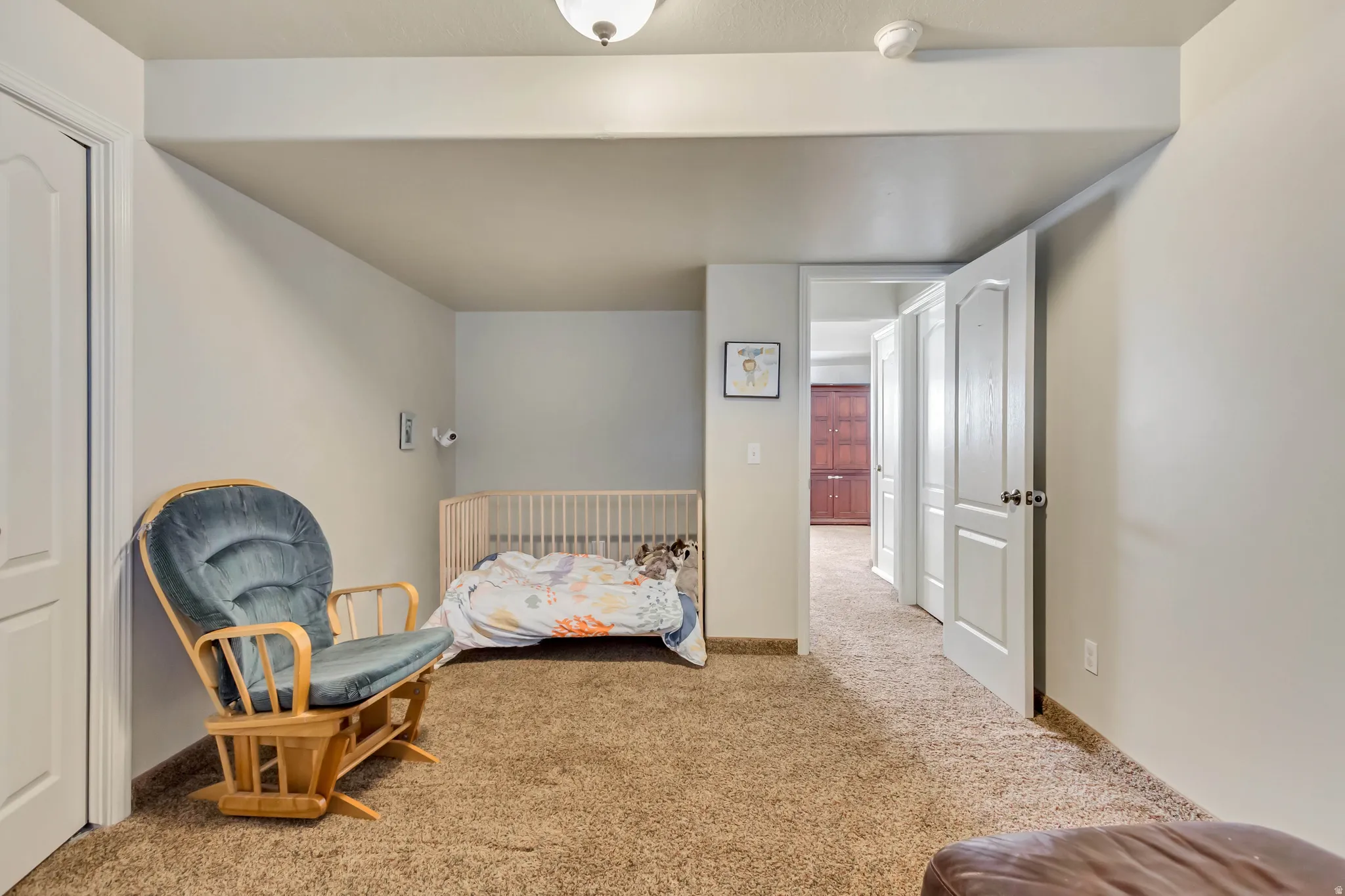 Carpeted room with white walls, featuring a white paneled door, recessed ceiling light, and a second doorway revealing a hallway with additional white doors