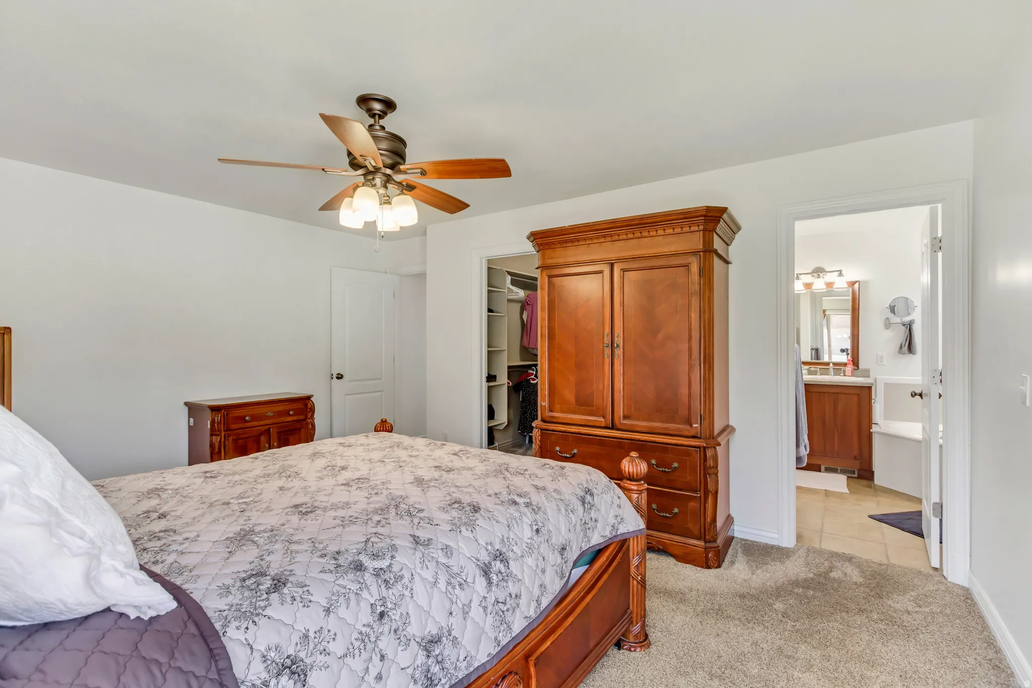 Carpeted bedroom featuring a ceiling fan with light fixture, white walls, and a walk-in closet