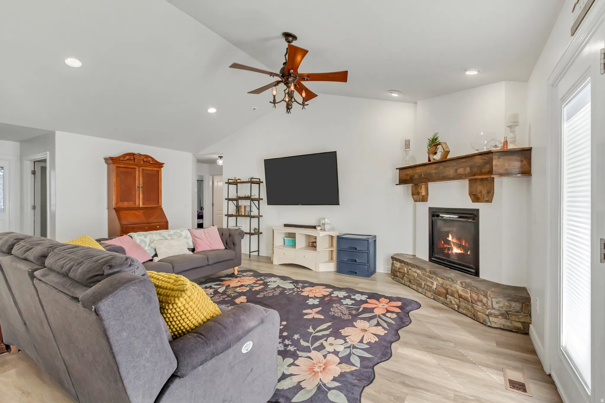Open-concept living area with vaulted ceilings, recessed lighting, wood-finish flooring, and a stone-front fireplace with a wood mantle