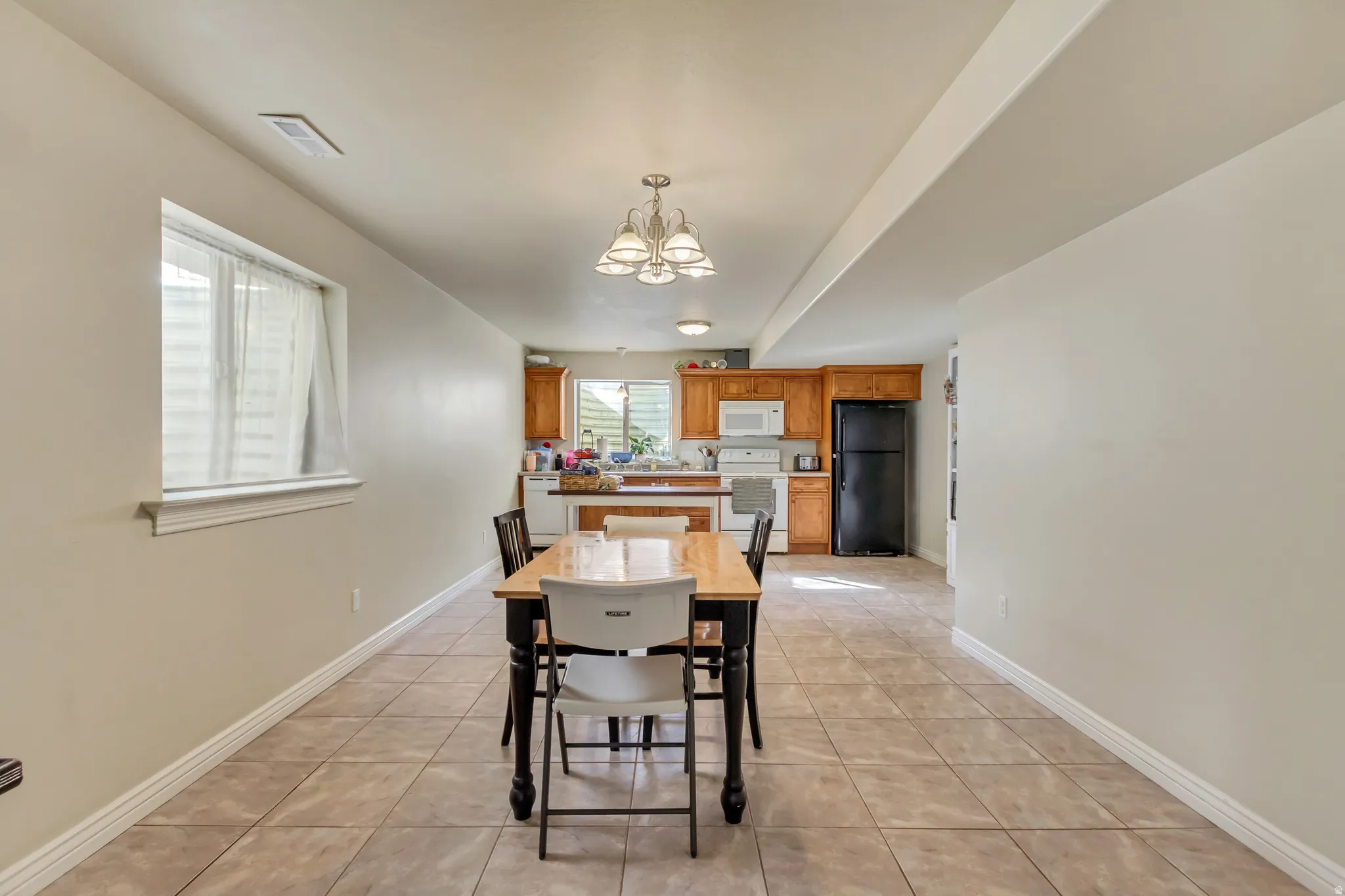 Open-concept kitchen and dining area featuring tile flooring, a window with blinds, wood cabinetry, a white built-in microwave, and a black refrigerator