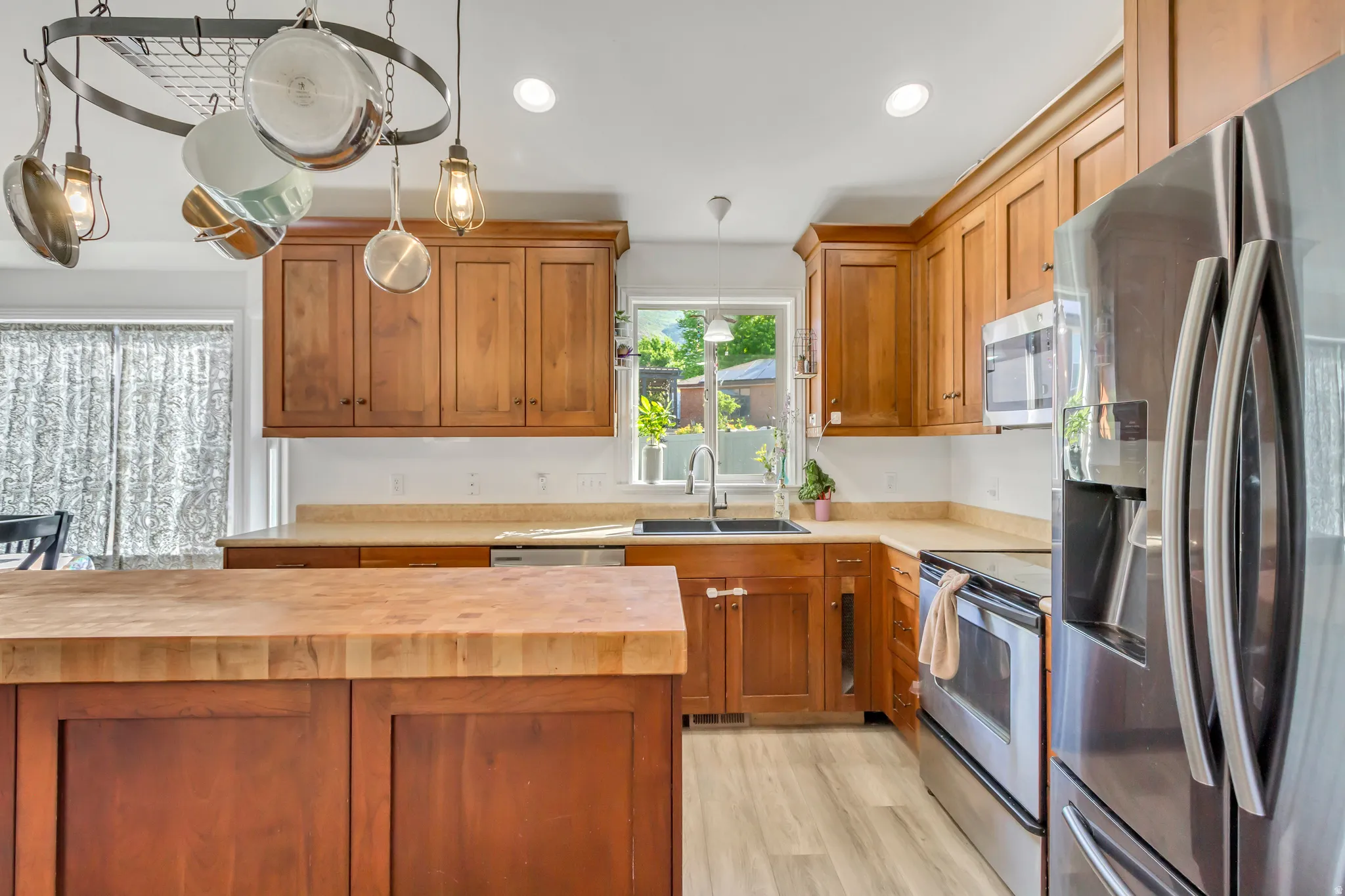 Kitchen featuring wood cabinetry, stainless steel appliances, a wood-finish island, light-toned countertops, and light wood-finish flooring