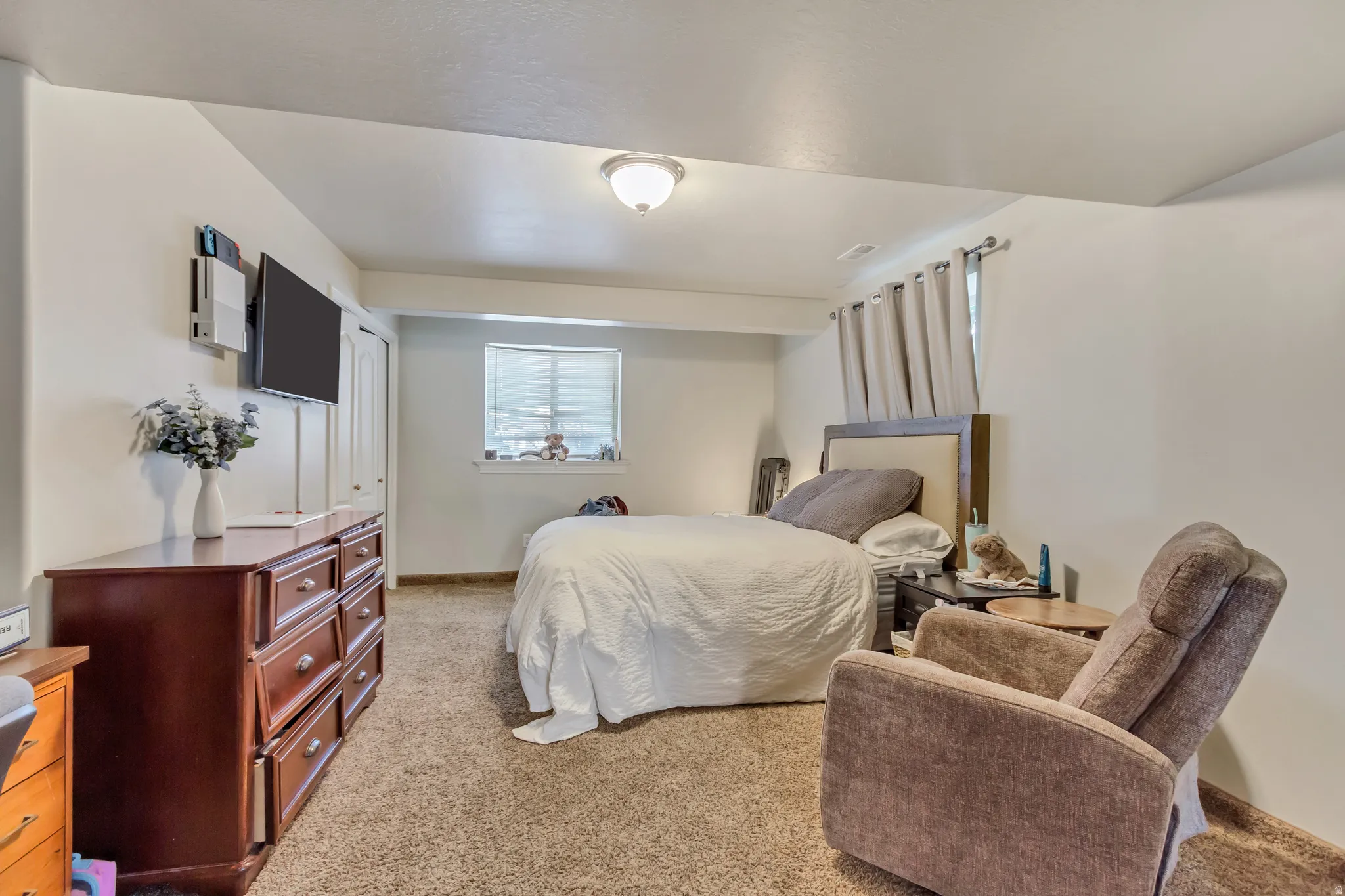 Carpeted room featuring a ceiling-mounted light fixture, white walls, and a window with blinds and curtains