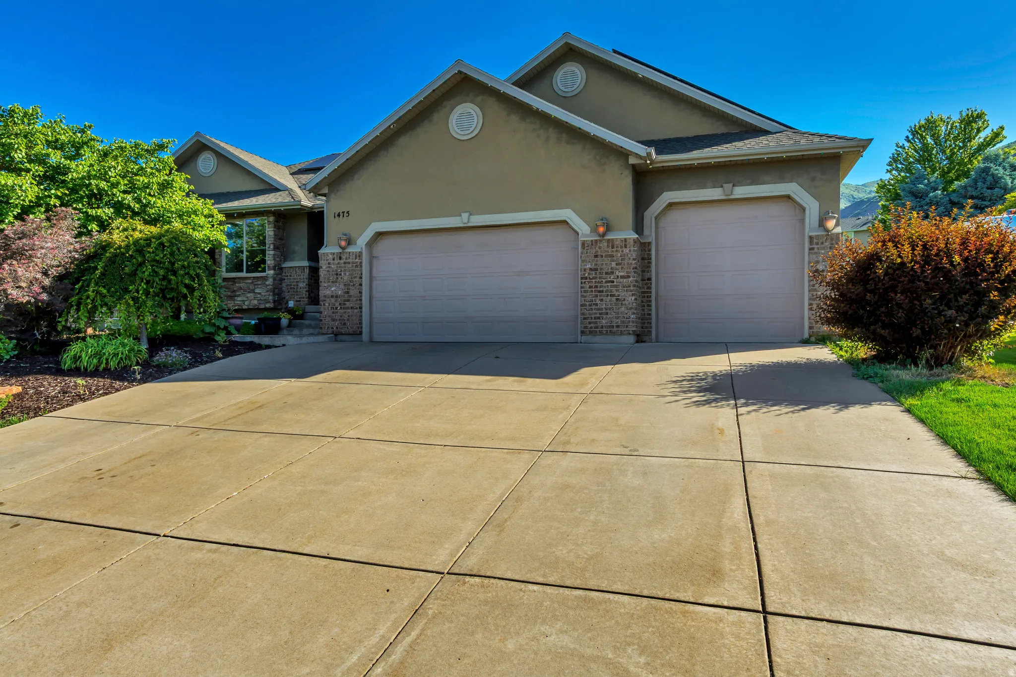 Stucco and brick facade residence featuring a two-car garage with individual doors, a concrete driveway, and established front landscaping