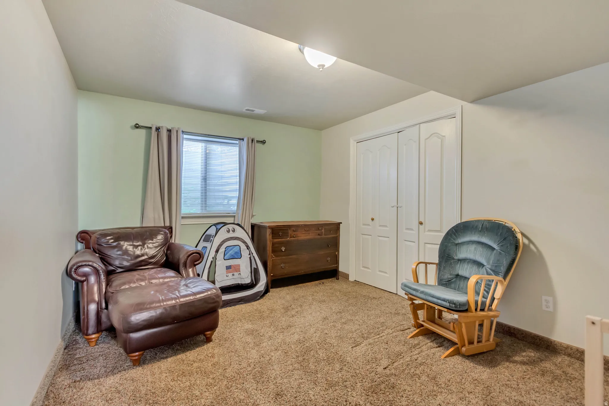 Carpeted room featuring a window with curtains, light green accent wall, white bi-fold closet doors, and recessed lighting