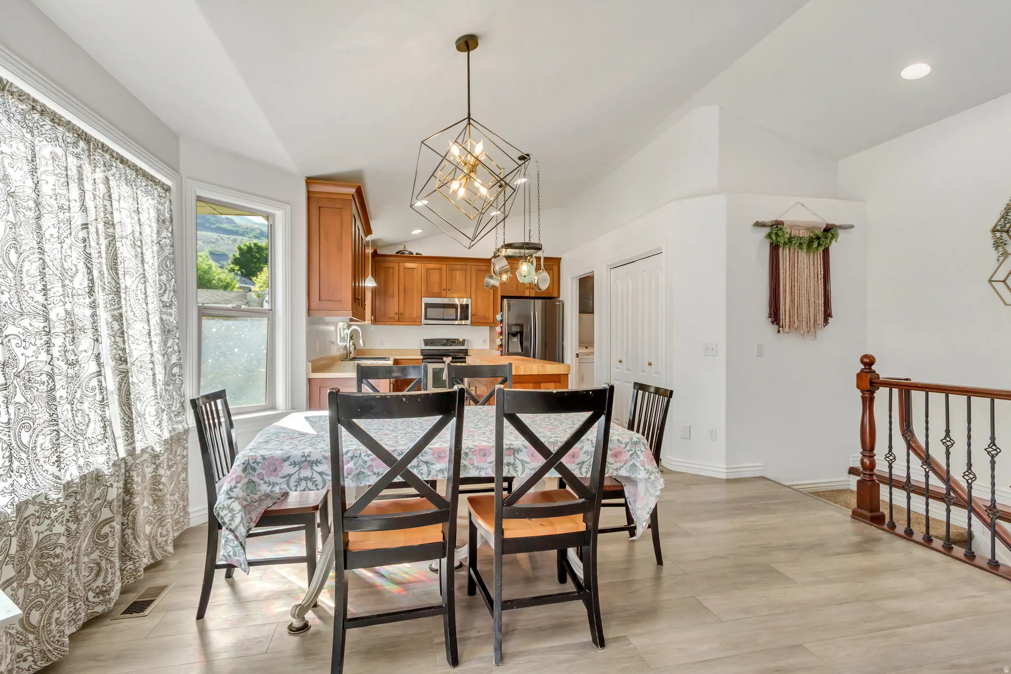 Dining area featuring a contemporary geometric pendant light fixture, wood-finish flooring, and a kitchen with warm-toned cabinetry, stainless steel appliances, and a central island