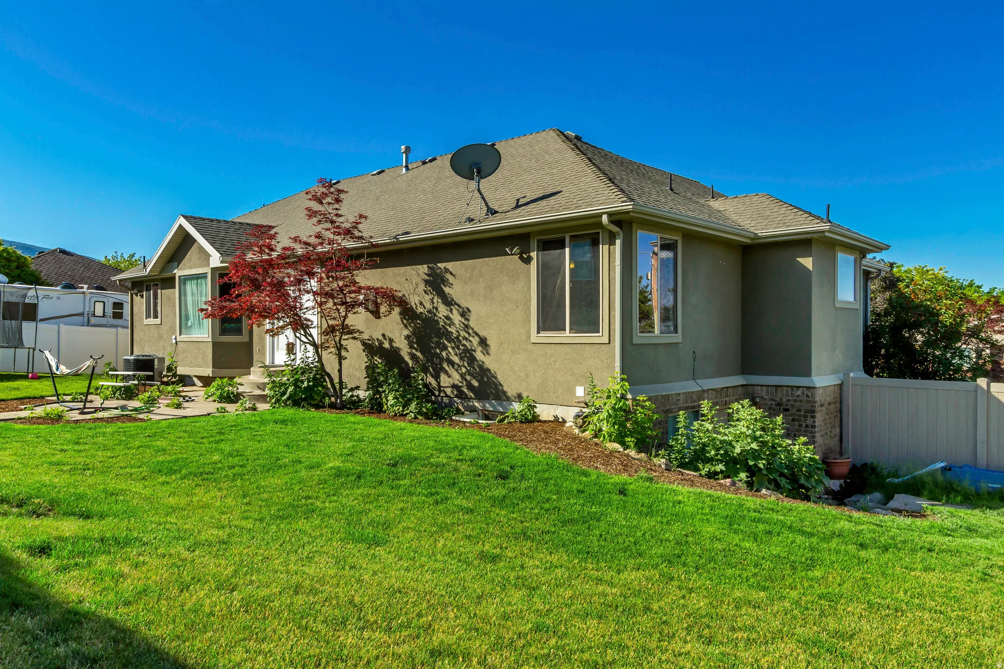 Exterior featuring stucco siding, a composition shingle roof, bay windows, and a landscaped yard with mature plantings